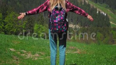 一个年轻的高加索女人带着背包和太阳镜站在山顶上举起双手。 概念
